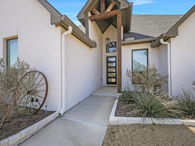 view of exterior entry featuring roof with shingles and brick siding