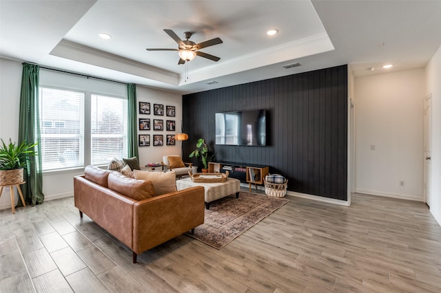 living room featuring ceiling fan, ornamental molding, a tray ceiling, and light hardwood / wood-style flooring