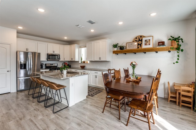 kitchen featuring stainless steel appliances, a kitchen bar, white cabinets, and light stone counters