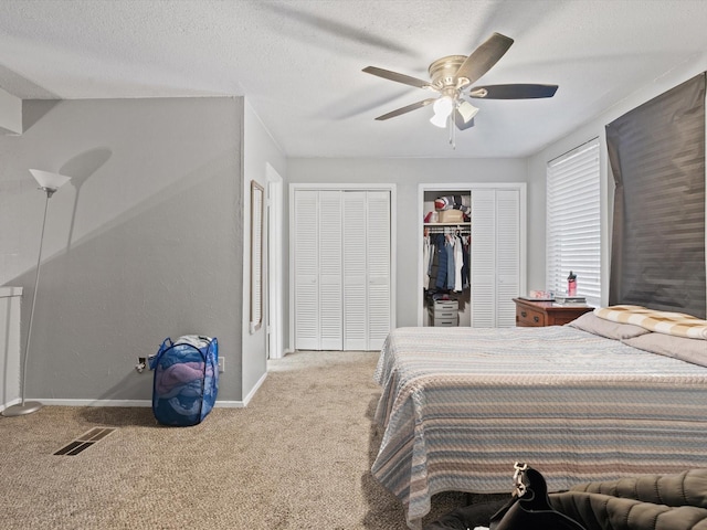 bedroom featuring ceiling fan, two closets, a textured ceiling, and carpet flooring