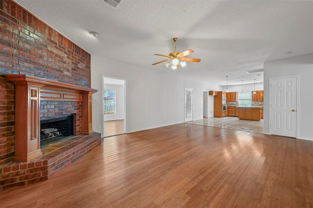2305 Buckeye Dr, Mesquite, TX 75181 - unfurnished living room with a ceiling fan, light wood-style floors, a textured ceiling, a brick fireplace, and healthy amount of natural light