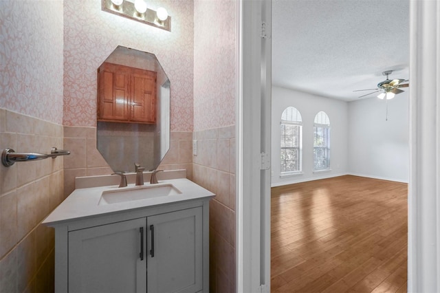 bathroom featuring ceiling fan, tile walls, hardwood / wood-style floors, vanity, and a textured ceiling