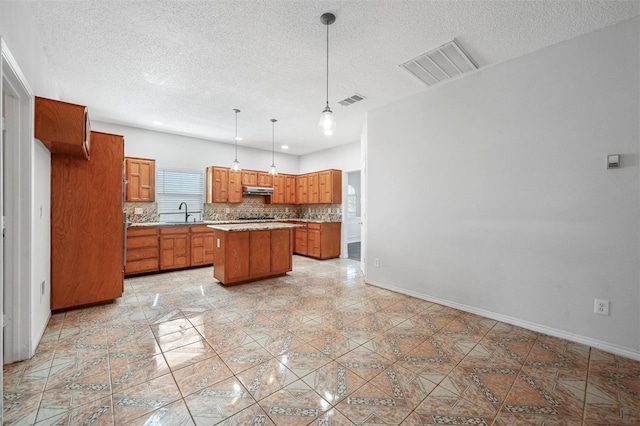 2305 Buckeye Dr, Mesquite, TX 75181 - kitchen featuring brown cabinets, a textured ceiling, a kitchen island, backsplash, and under cabinet range hood
