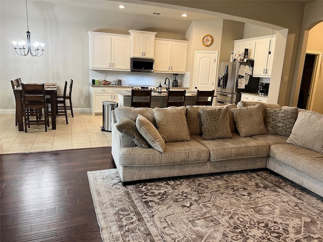 living room with baseboards, arched walkways, an inviting chandelier, light wood-type flooring, and recessed lighting