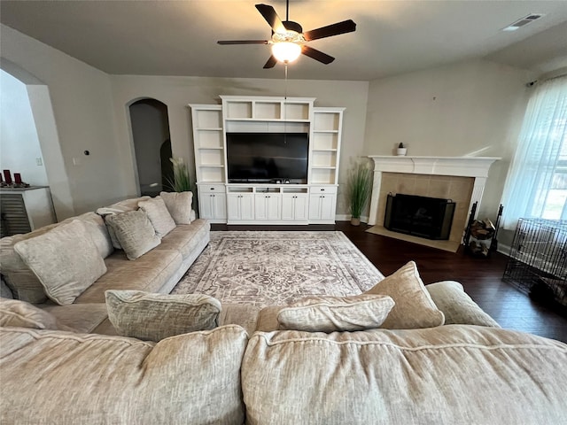 living area featuring arched walkways, dark wood-style flooring, a fireplace, visible vents, and a ceiling fan