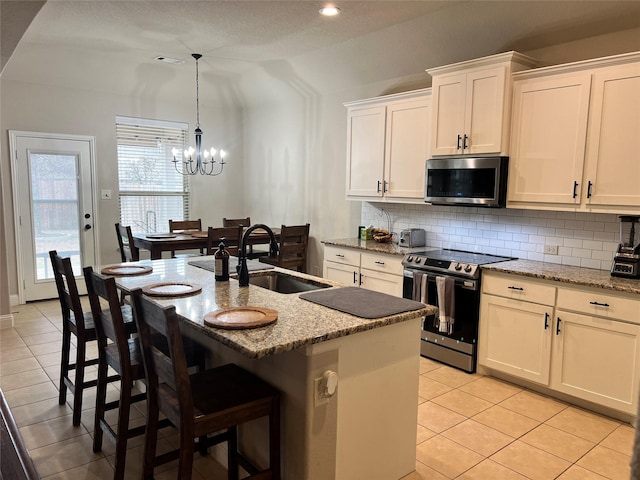 kitchen with stainless steel appliances, light stone counters, a kitchen island with sink, and white cabinets