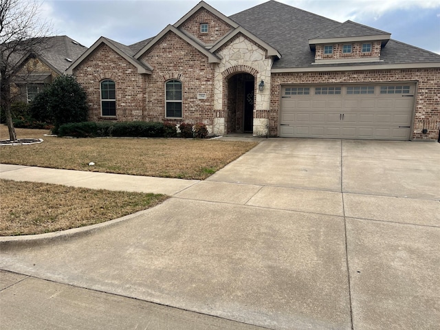 french country style house featuring brick siding, roof with shingles, concrete driveway, stone siding, and a front lawn