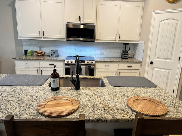 kitchen with appliances with stainless steel finishes, white cabinets, decorative backsplash, and light stone counters