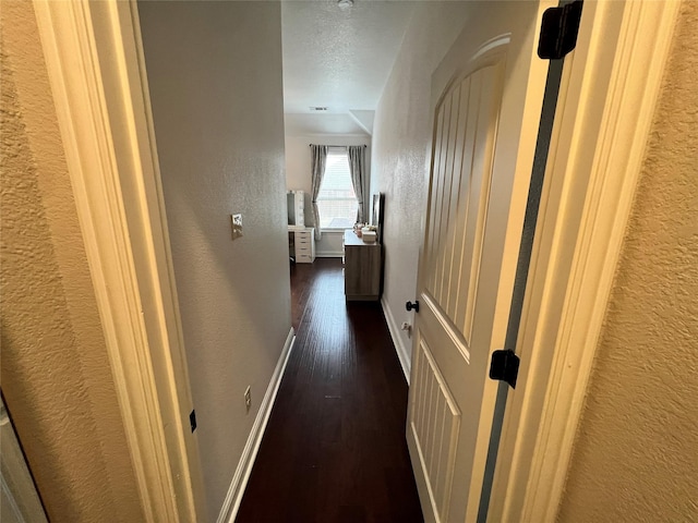 hall with dark wood-style floors, a textured wall, and baseboards