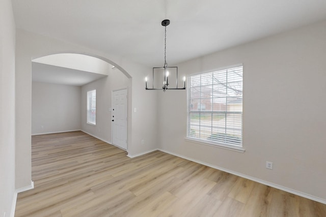 unfurnished room featuring a healthy amount of sunlight, a notable chandelier, and light wood-type flooring