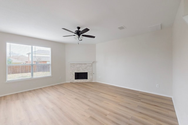 unfurnished living room with a stone fireplace, ceiling fan, and light hardwood / wood-style flooring