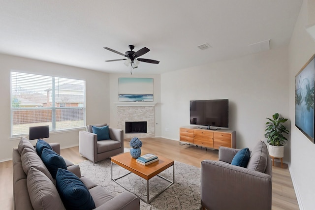 living room featuring a stone fireplace, ceiling fan, and light wood-type flooring