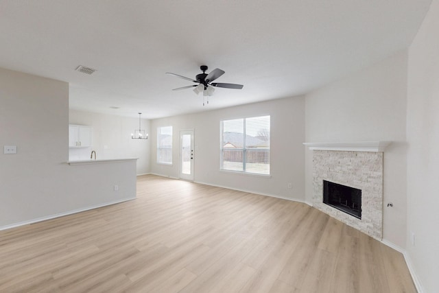 unfurnished living room with a stone fireplace, ceiling fan with notable chandelier, and light hardwood / wood-style floors