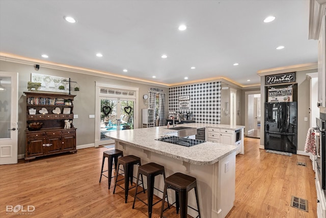 kitchen featuring visible vents, white cabinets, an island with sink, a breakfast bar area, and black appliances