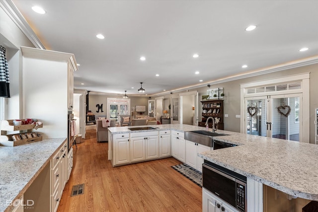 kitchen featuring light wood-style flooring, ornamental molding, open floor plan, white cabinets, and a sink