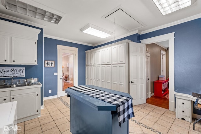 kitchen with a sink, white cabinets, crown molding, and light tile patterned flooring