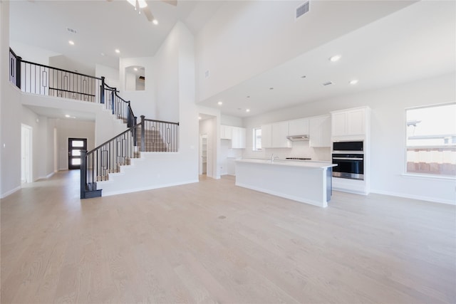 unfurnished living room with light wood-style floors, a ceiling fan, visible vents, stairway, and baseboards