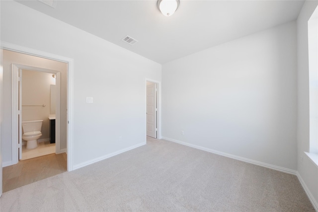 unfurnished bedroom featuring ensuite bathroom, baseboards, carpet, and visible vents