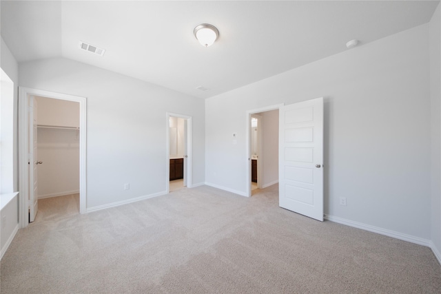unfurnished bedroom featuring vaulted ceiling, visible vents, light carpet, a walk in closet, and baseboards