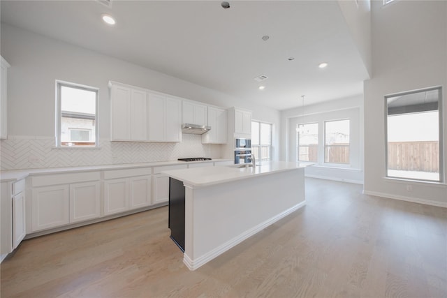 kitchen featuring white cabinets, under cabinet range hood, backsplash, gas cooktop, and built in microwave