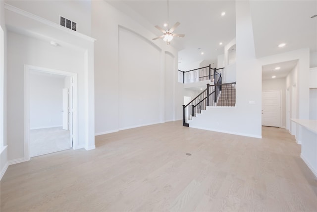 unfurnished living room featuring a towering ceiling, light wood-type flooring, stairway, visible vents, and ceiling fan