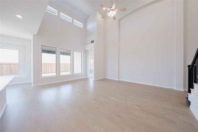 unfurnished living room with ceiling fan, stairway, a high ceiling, light wood finished floors, and baseboards