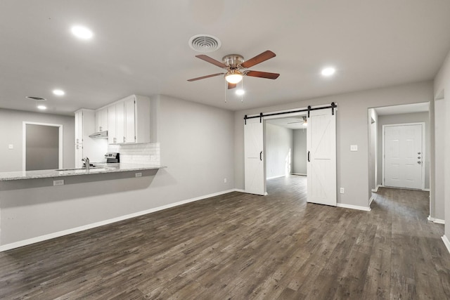 unfurnished living room with a barn door, dark hardwood / wood-style floors, sink, and ceiling fan