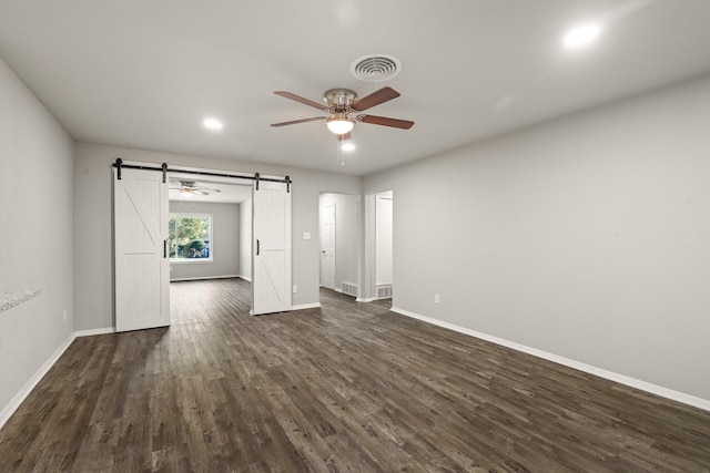 unfurnished bedroom featuring a barn door, dark hardwood / wood-style floors, and ceiling fan