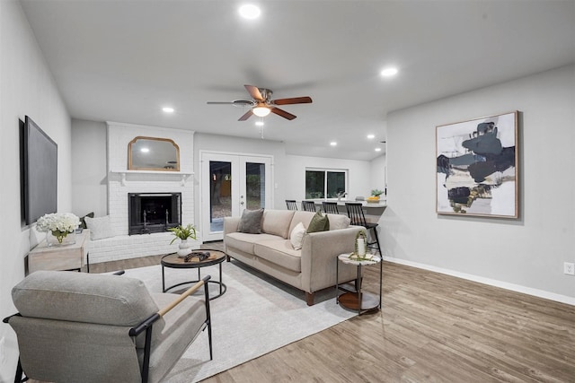 living room featuring hardwood / wood-style floors, french doors, a brick fireplace, and ceiling fan