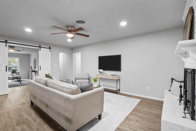 living room with ceiling fan, a barn door, hardwood / wood-style floors, and a brick fireplace