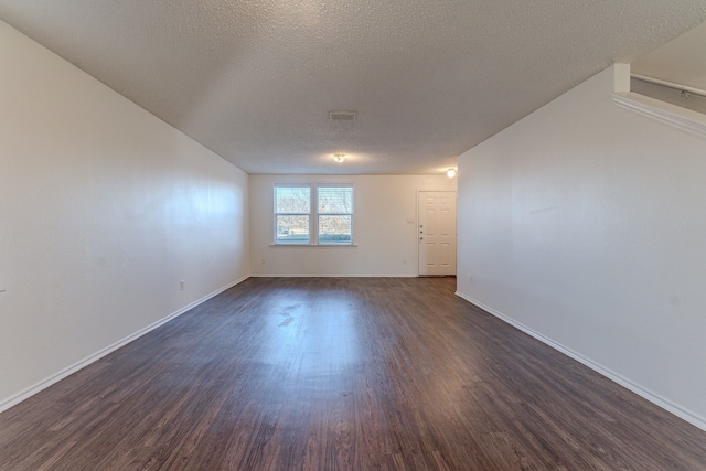 unfurnished room with visible vents, dark wood finished floors, a textured ceiling, and baseboards