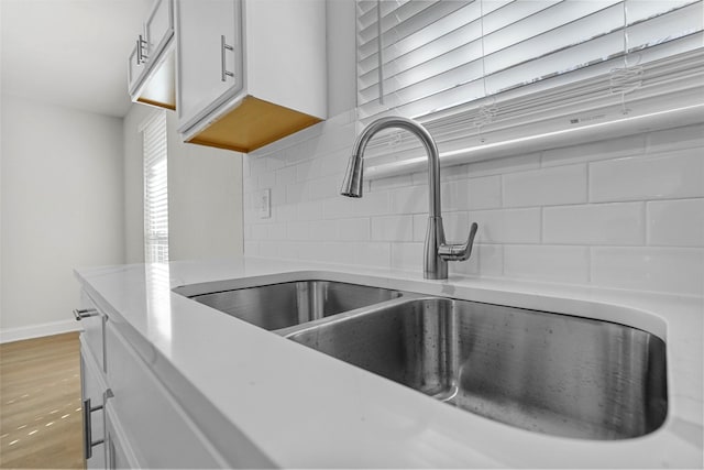 details featuring sink, decorative backsplash, wood-type flooring, and white cabinets