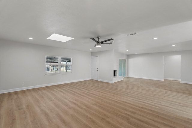 unfurnished living room with light hardwood / wood-style flooring, a skylight, a fireplace, and ceiling fan