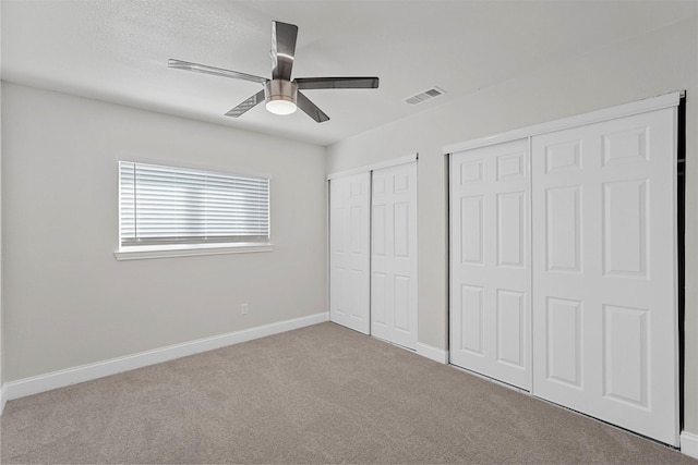 unfurnished bedroom featuring ceiling fan, light colored carpet, and two closets