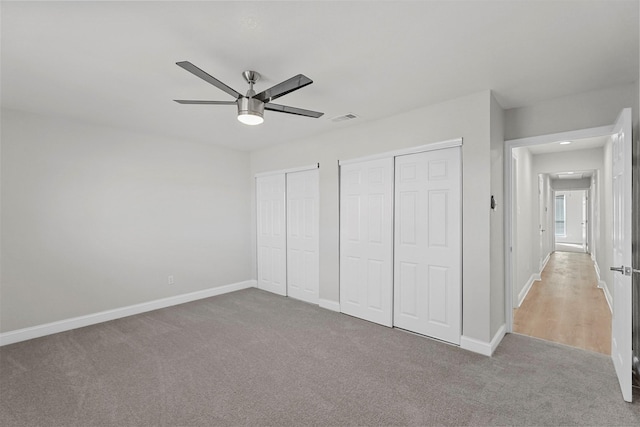 unfurnished bedroom with light carpet, two closets, and ceiling fan