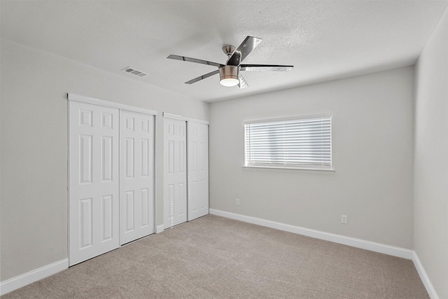 unfurnished bedroom with light carpet, ceiling fan, a textured ceiling, and multiple closets