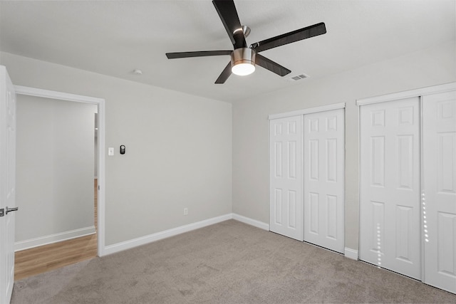 unfurnished bedroom with ceiling fan, light colored carpet, and multiple closets