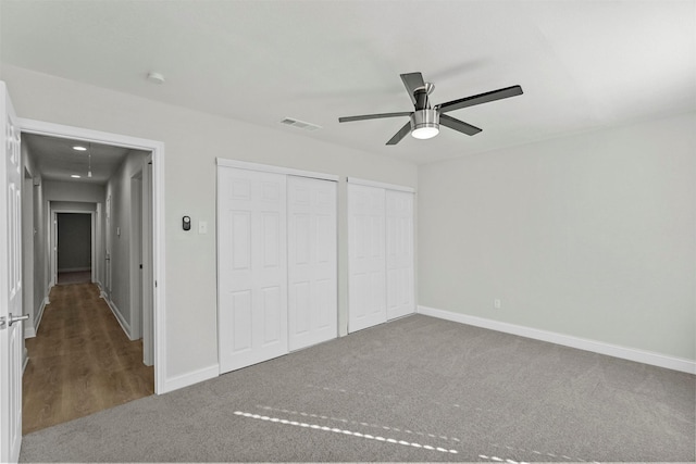 unfurnished bedroom featuring ceiling fan, dark carpet, and two closets