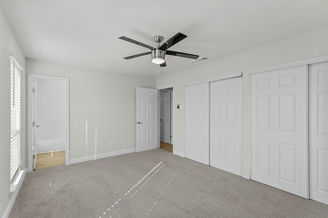 unfurnished bedroom featuring ceiling fan, light colored carpet, connected bathroom, and two closets