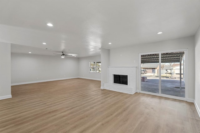 unfurnished living room featuring ceiling fan, light hardwood / wood-style floors, and a brick fireplace