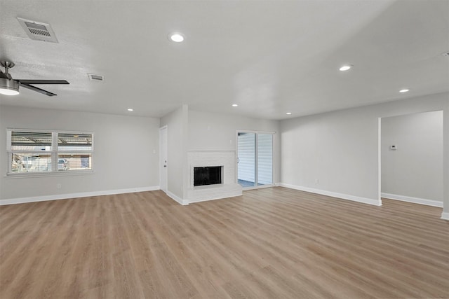 unfurnished living room featuring ceiling fan, a brick fireplace, and light wood-type flooring