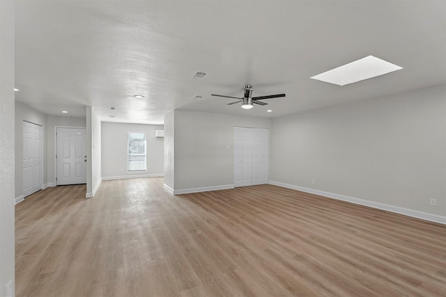 empty room featuring ceiling fan, a skylight, and light wood-type flooring