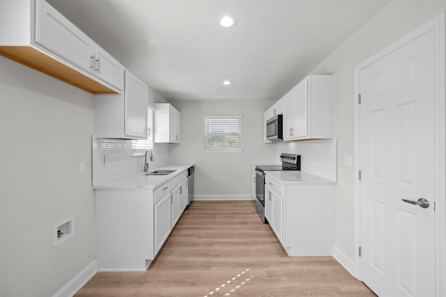 kitchen featuring sink, white cabinetry, stainless steel appliances, light hardwood / wood-style floors, and backsplash