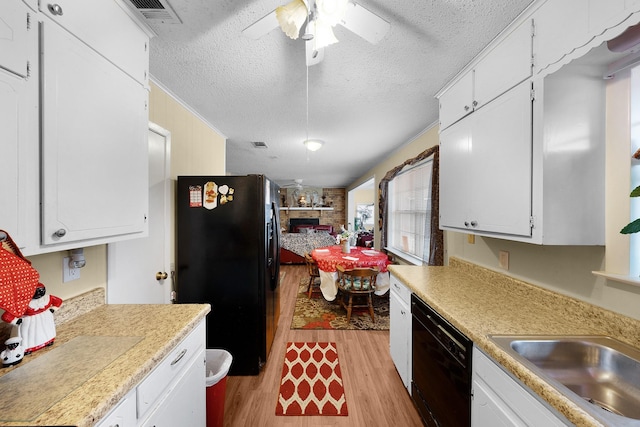 kitchen with a stone fireplace, black appliances, white cabinets, and light wood-type flooring