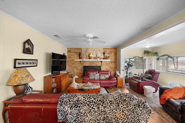 living room with crown molding, a textured ceiling, ceiling fan, a fireplace, and hardwood / wood-style floors