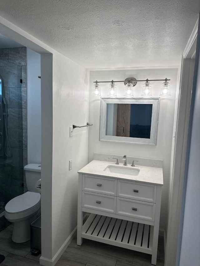 bathroom featuring a tile shower, vanity, a textured ceiling, and toilet