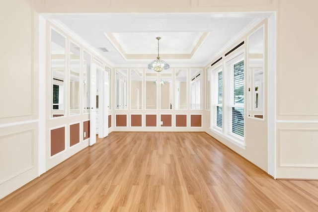 unfurnished room featuring a raised ceiling, wood-type flooring, ornamental molding, and an inviting chandelier