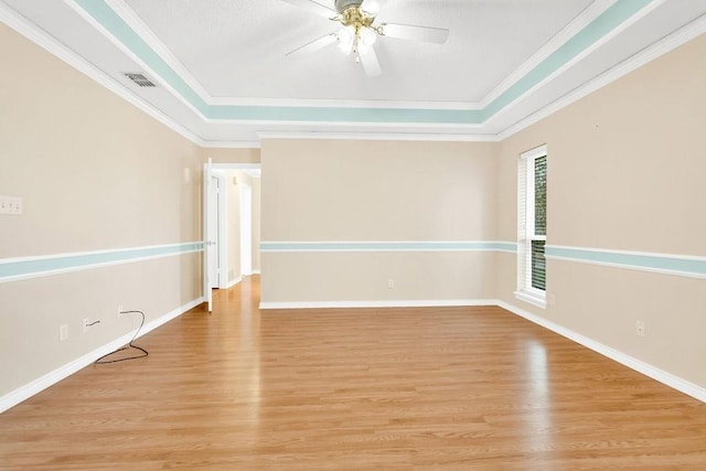 spare room with crown molding, a tray ceiling, and light wood-type flooring