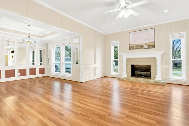 unfurnished living room featuring crown molding, ceiling fan with notable chandelier, a brick fireplace, and light wood-type flooring