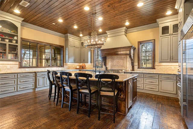 kitchen featuring wood ceiling, light stone counters, a kitchen island with sink, and a breakfast bar area